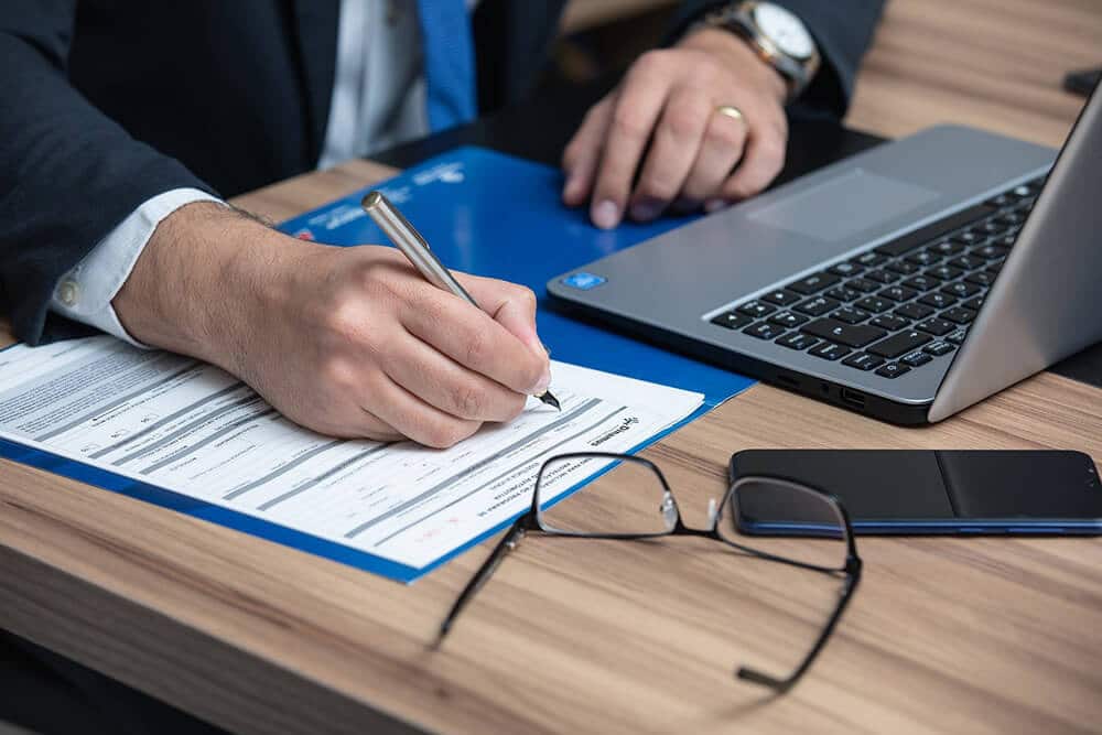 Person signing documents next to computer